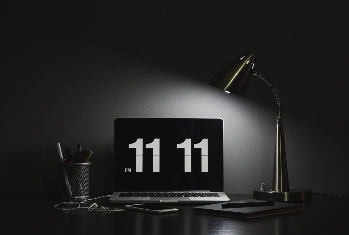 Moody desk workspace with laptop showing 11:11, desk lamp, and stationery