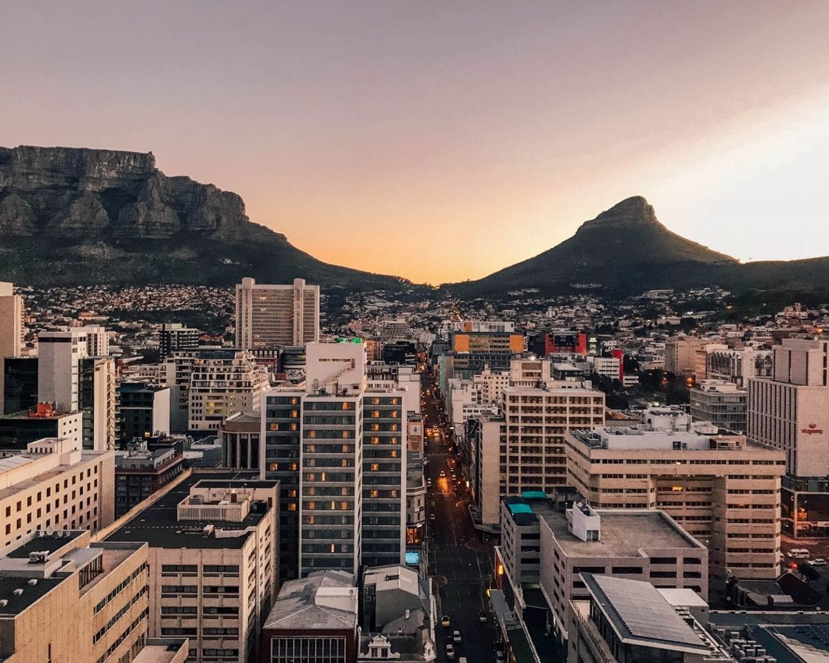 Cape Town city skyline at sunset with Table Mountain and Lions Head silhouetted against a warm golden sky